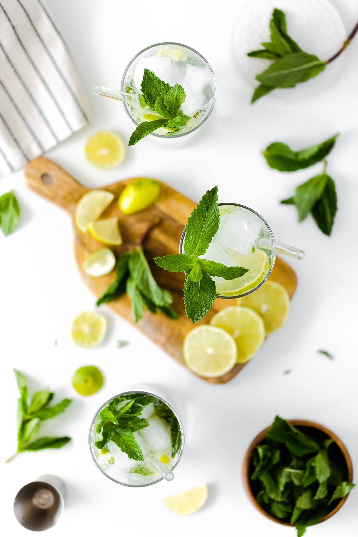 A wide overhead photo of mojitos on a white background with wooden board and a washcloth