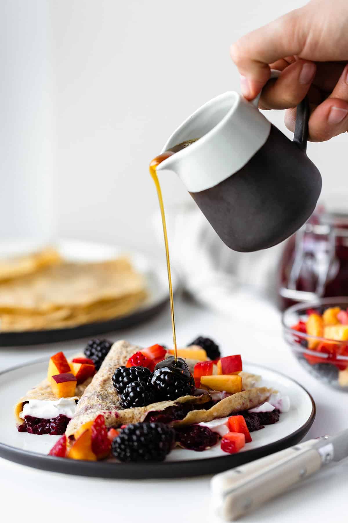 Maple syrup being poured over gluten-free crepes with Lavender Blackberry Jam