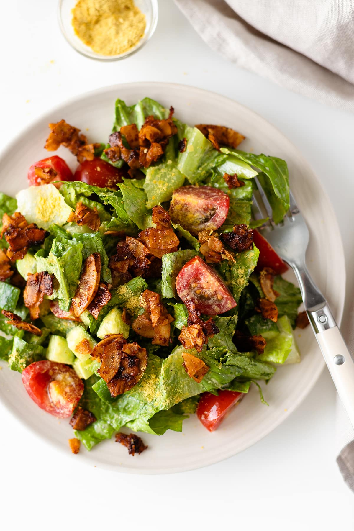 A green salad with romain, tomatoes, vegan coconut bacon and nutritional yeast - close up