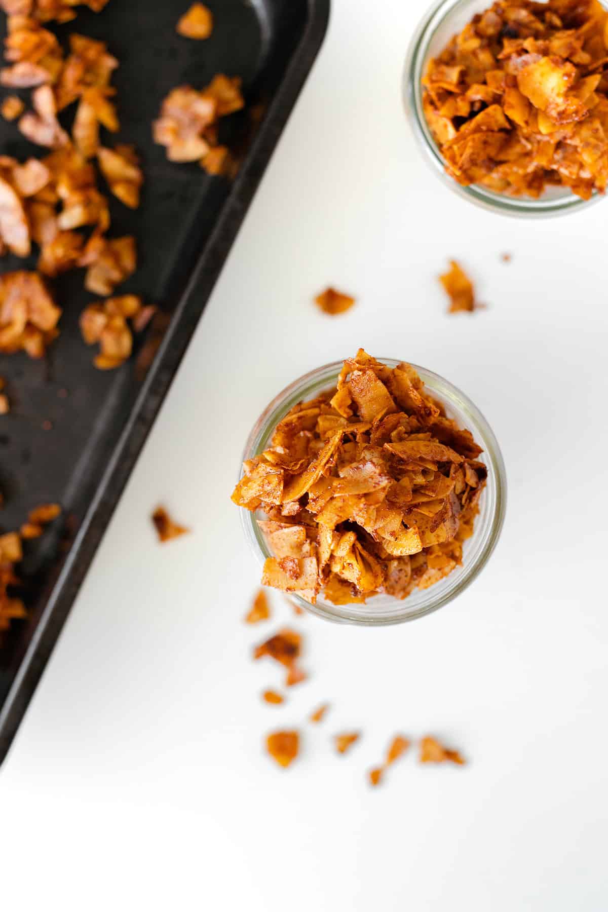 Overhead shot of vegan coconut bacon in a glass jar and on a baking pan