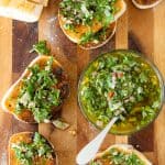 Sliced toasted baguette on a wooden cutting board, with chimichurri sauce in a glass bowl