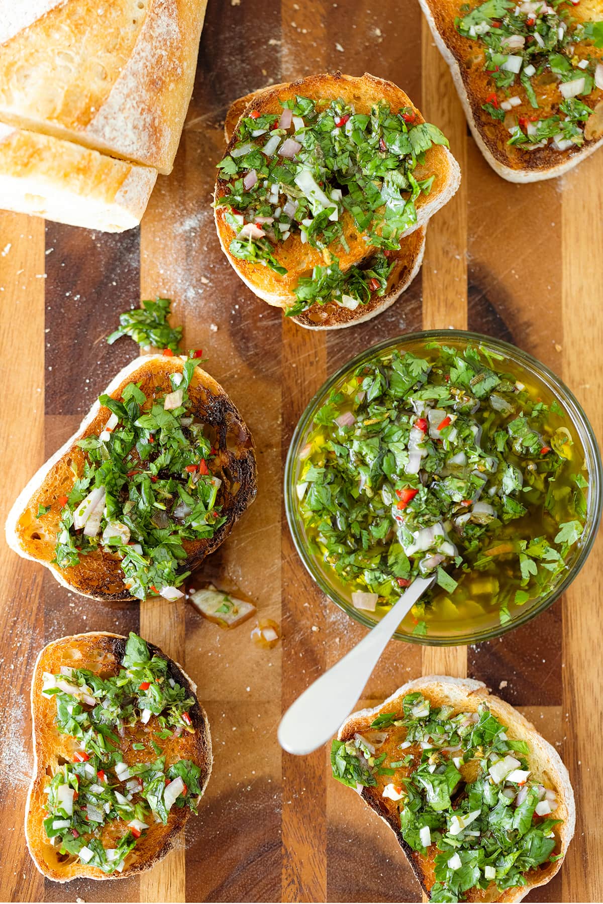 Sliced toasted baguette on a wooden cutting board, with chimichurri sauce in a glass bowl