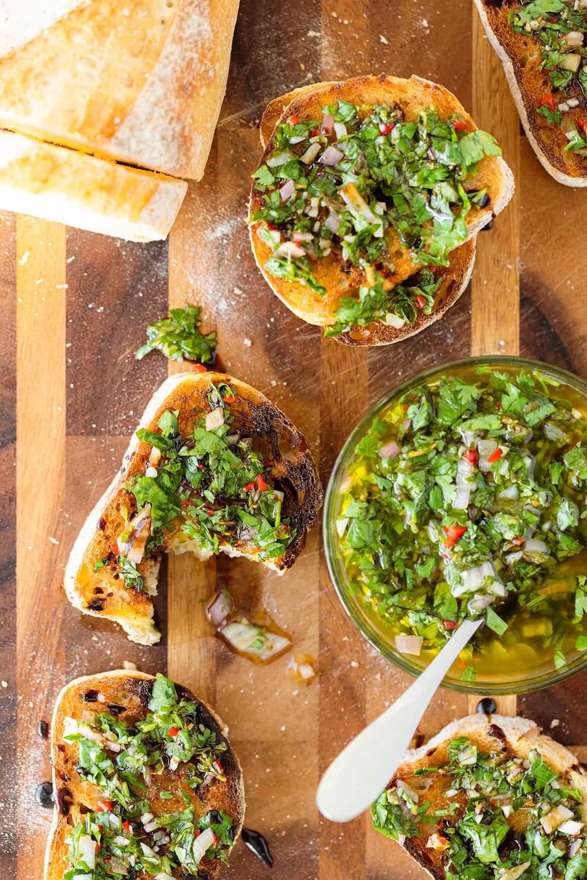 Sliced toasted baguette on a wooden cutting board, with chimichurri sauce and balsamic glaze