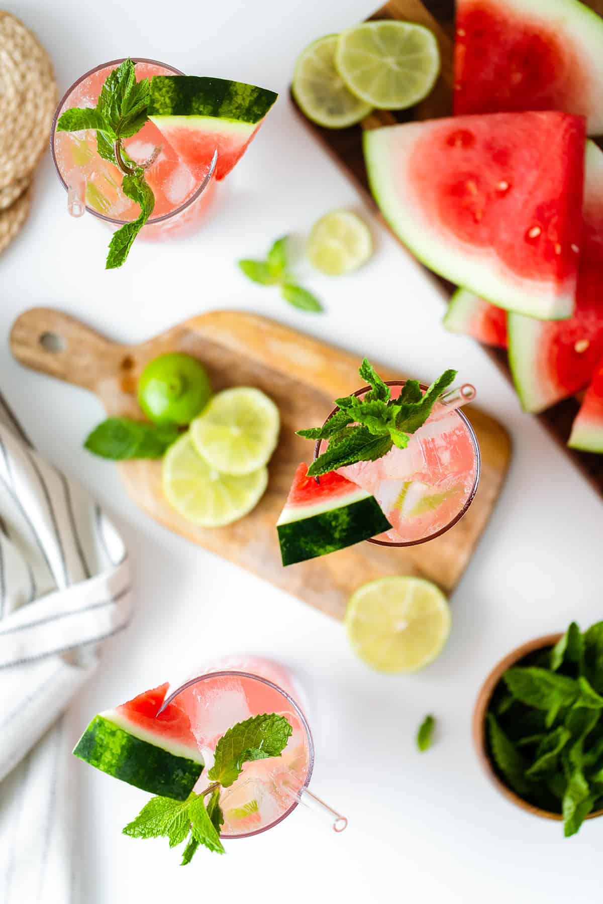 Watermelon Coconut Rum Cooler overhead shot, one drink on a small wooden cutting board, the other two on white table with watermelon slices on the right