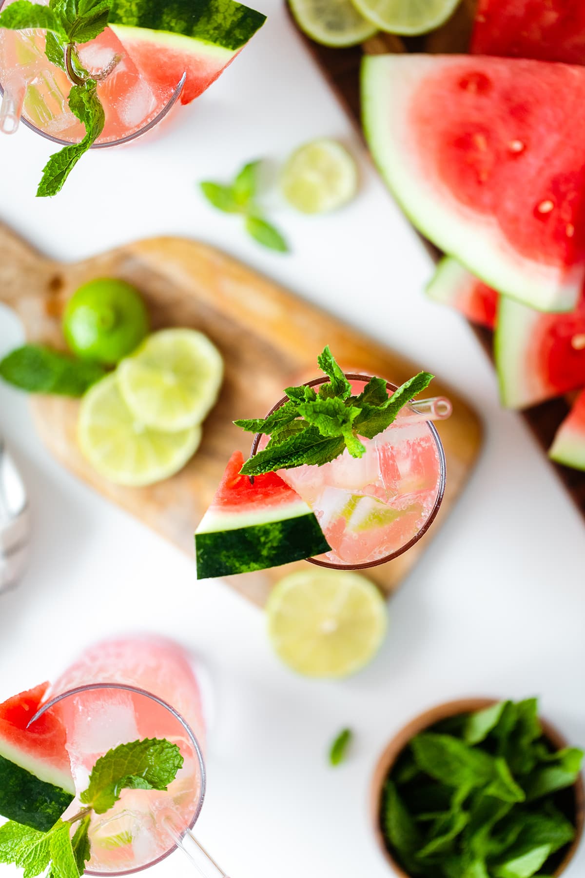 Watermelon Coconut Rum Cooler overhead shot, one drink on a small wooden cutting board, the other two on white table with watermelon slices on the right