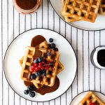 Basic Gluten-free Waffles with Tahini Chocolate Sauce and berries on a white plate and a white table cloth with black stripes