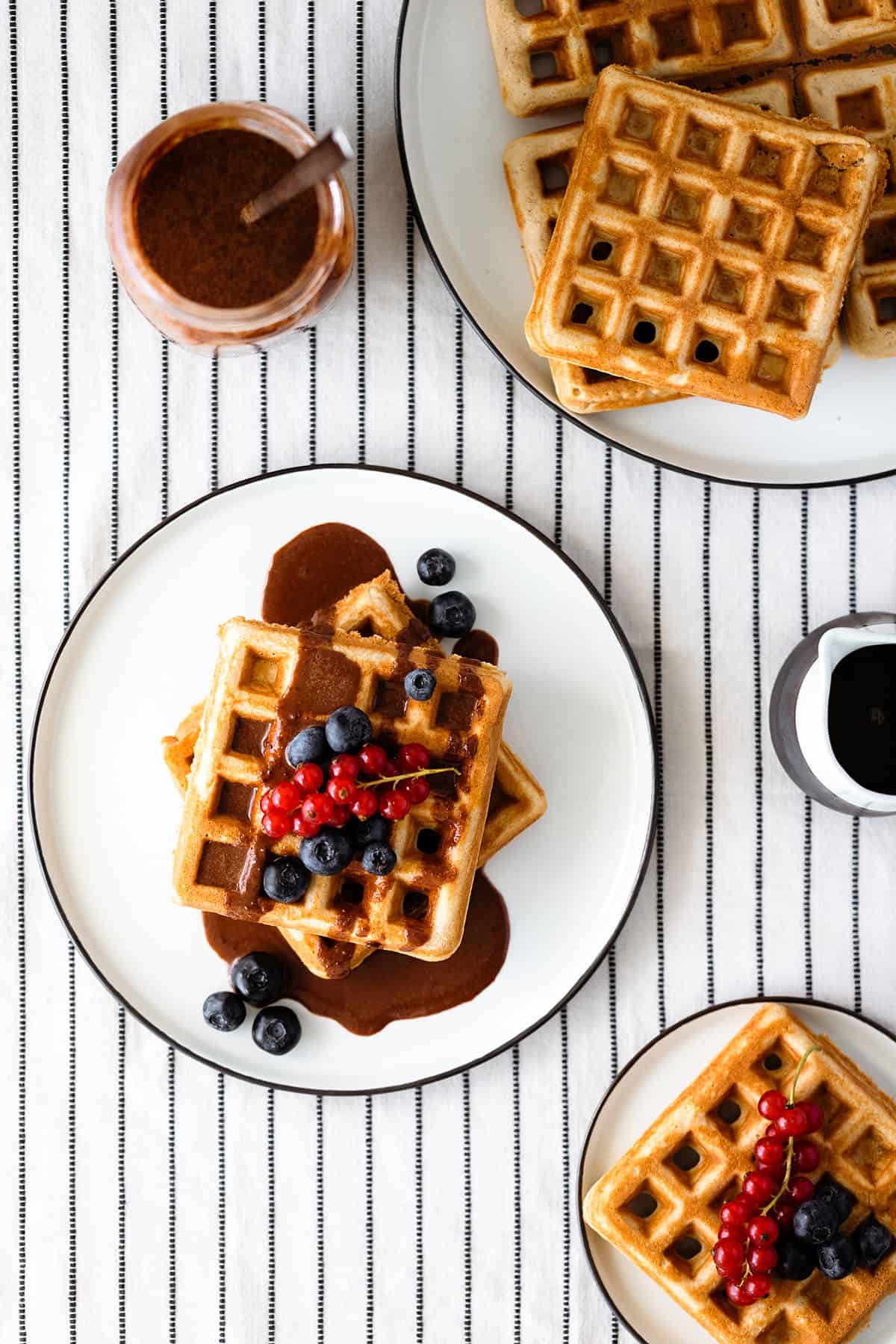 Basic Gluten-free Waffles with Tahini Chocolate Sauce and berries on a white plate and a white table cloth with black stripes