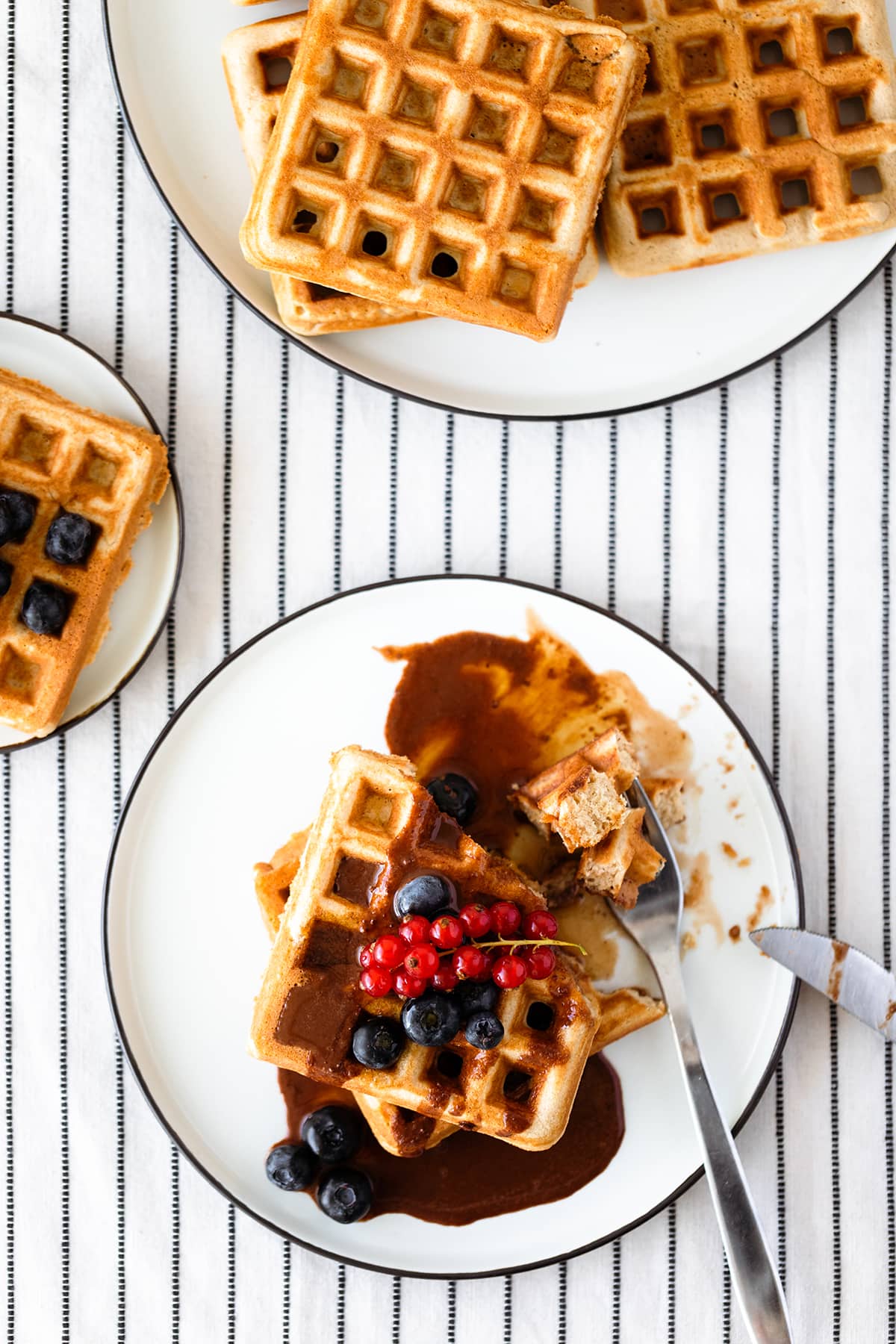 Basic Gluten-free Waffles with Tahini Chocolate Sauce and berries on a white plate and a white table cloth with black stripes