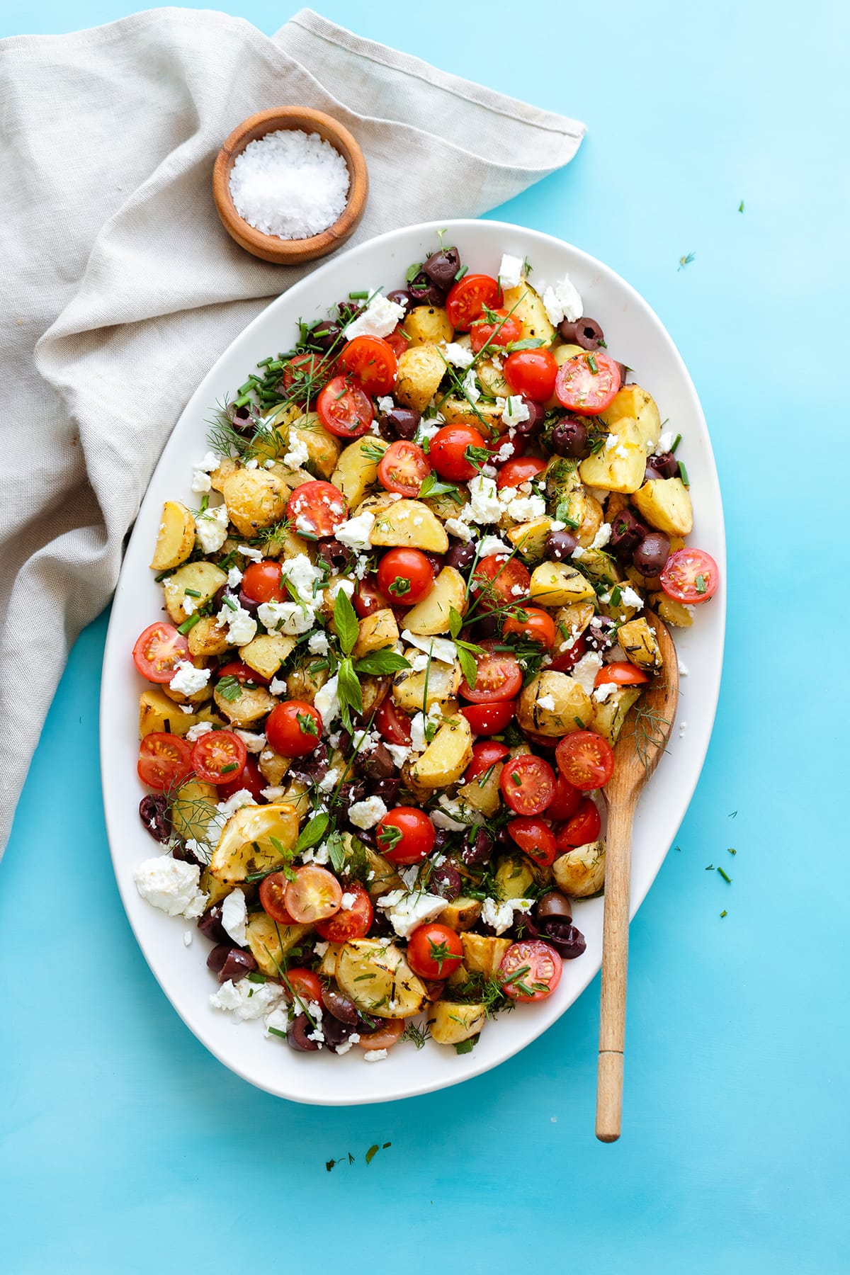 Greek Potato Salad with Feta, Olives, and fresh herbs on an oval platter. Bright blue background
