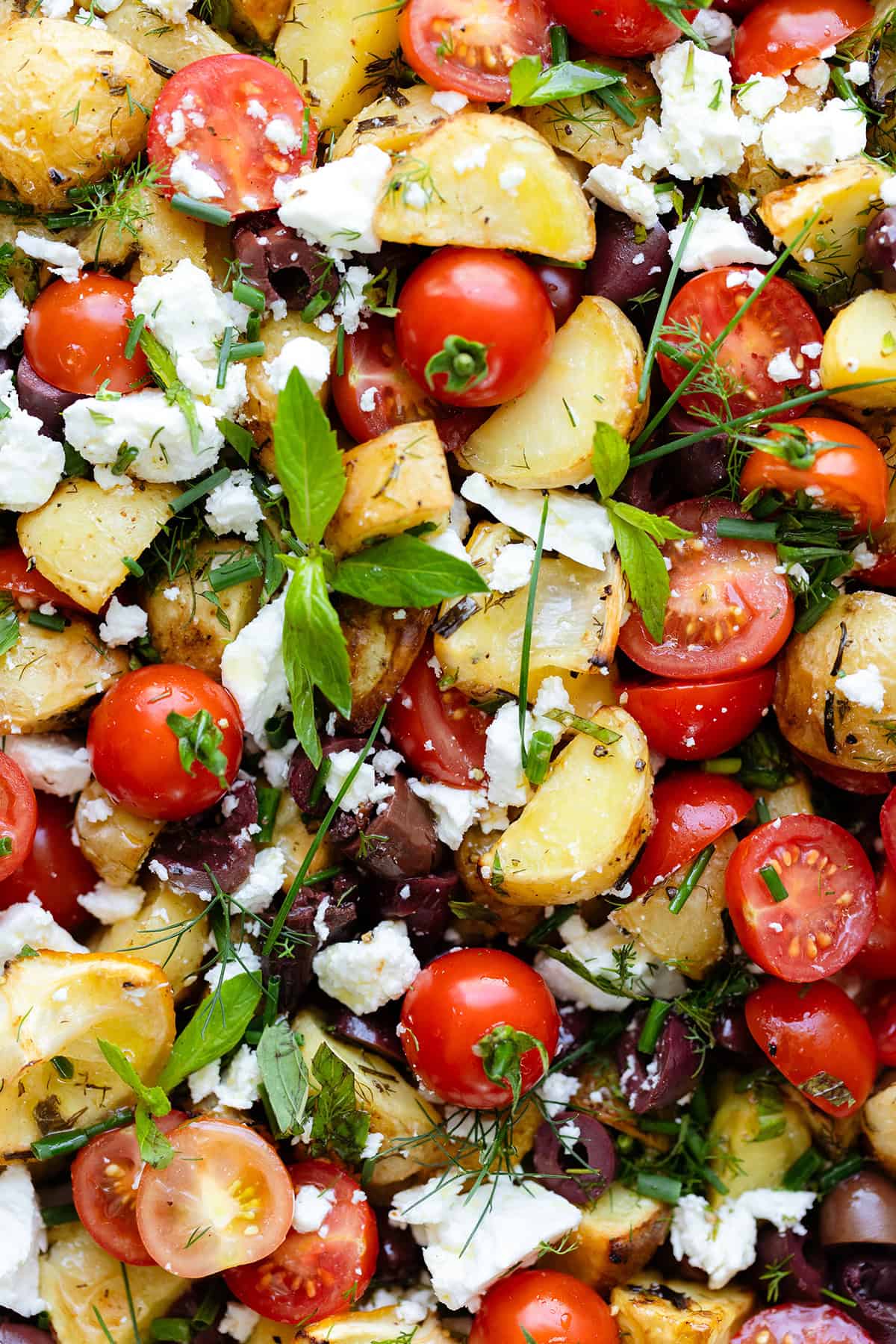 Greek Potato Salad with Feta, Olives, and fresh herbs on an oval platter. Close up photo.