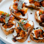 A photo of Butternut Squash Crostini with Goat Cheese and Fig Balsamic Glaze on a white plate