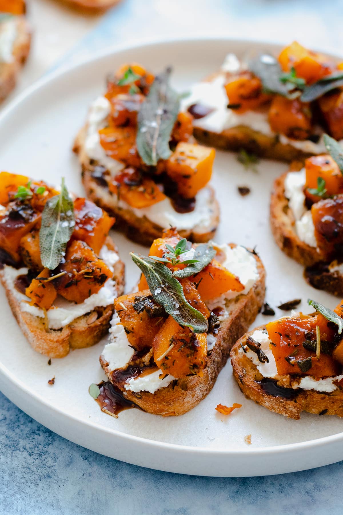 A photo of Butternut Squash Crostini with Goat Cheese and Fig Balsamic Glaze on a white plate