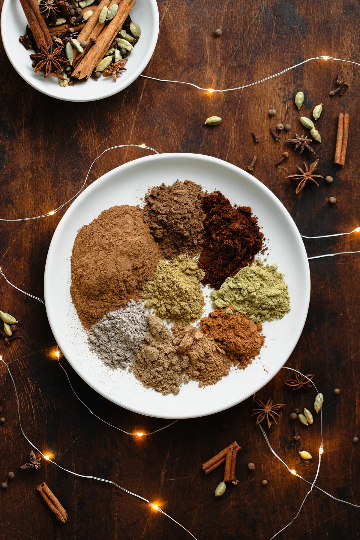 A photo of all the spices used in the Christmas Spice Blend on a white plate. On a dark wooden background.