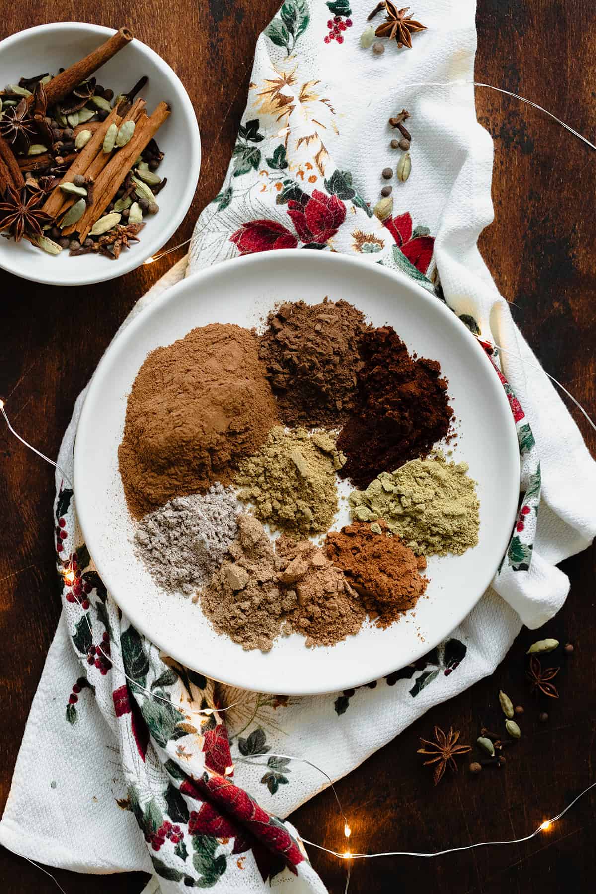 A photo of all the spices used in the Christmas Spice Blend on a white plate. On a dark wooden background.