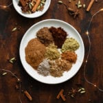 A photo of all the spices used in the Christmas Spice Blend on a white plate. On a dark wooden background and fairy lights.