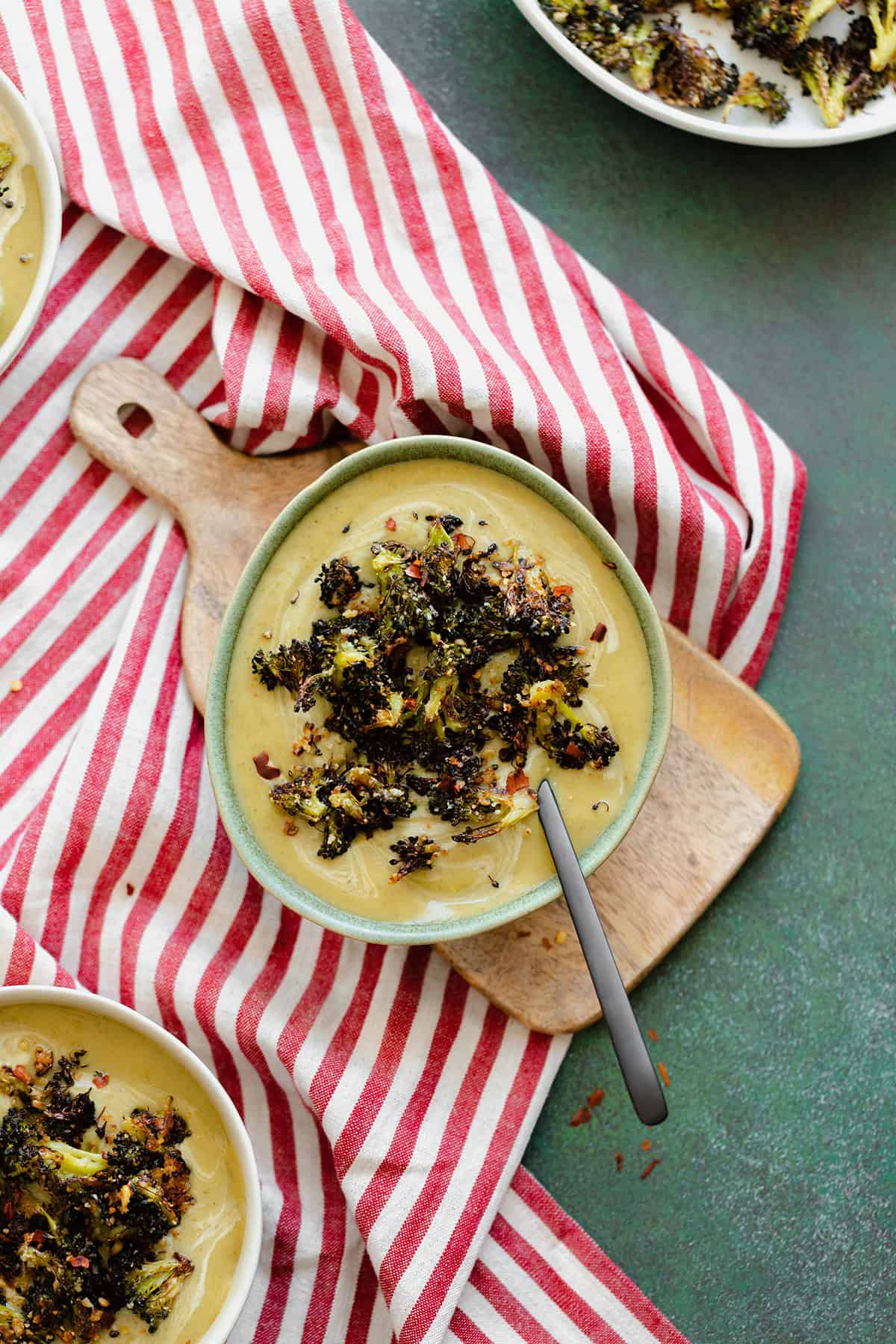 An overhead shot of Cream of Broccoli Soup with Roasted Broccoli Croutons on a striped red and white tea towel and green background