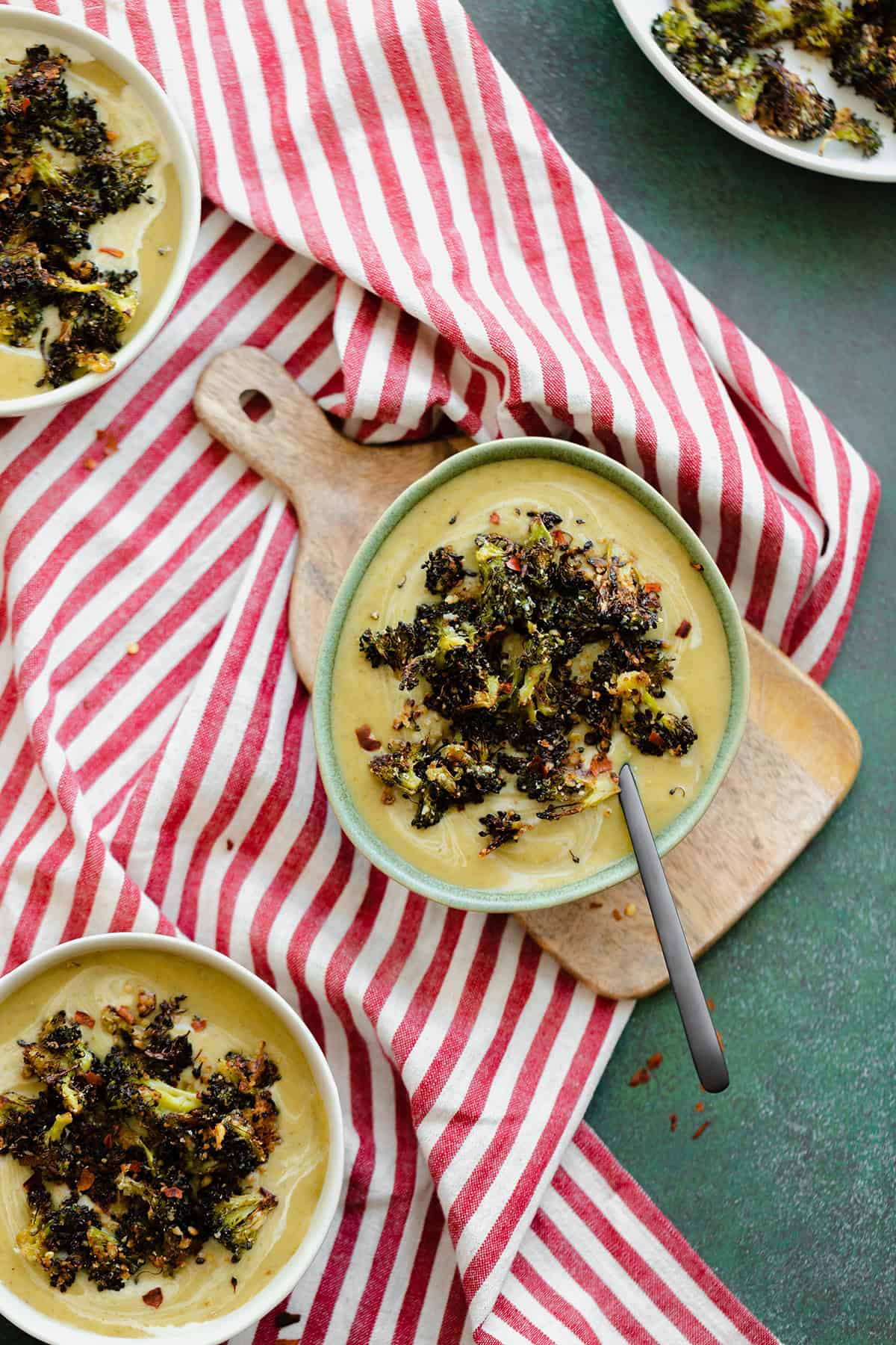 An overhead shot of Cream of Broccoli Soup with Roasted Broccoli Croutons on a striped red and white tea towel and green background