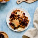 An overhead photo fo Gluten-Free Apple Butter Waffles with apples, cranberries, and walnuts on blue background.