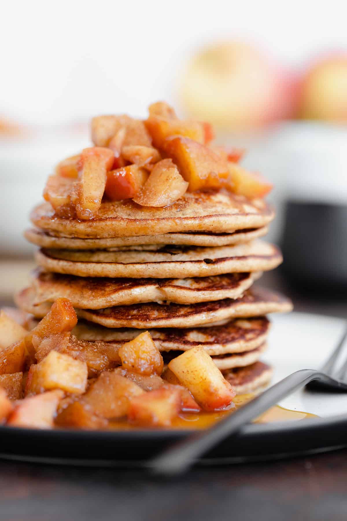 A straight on photo of Chocolate Chip Apple Cider Pancakes with Stewed Apples on a white plate and dark wooden background.