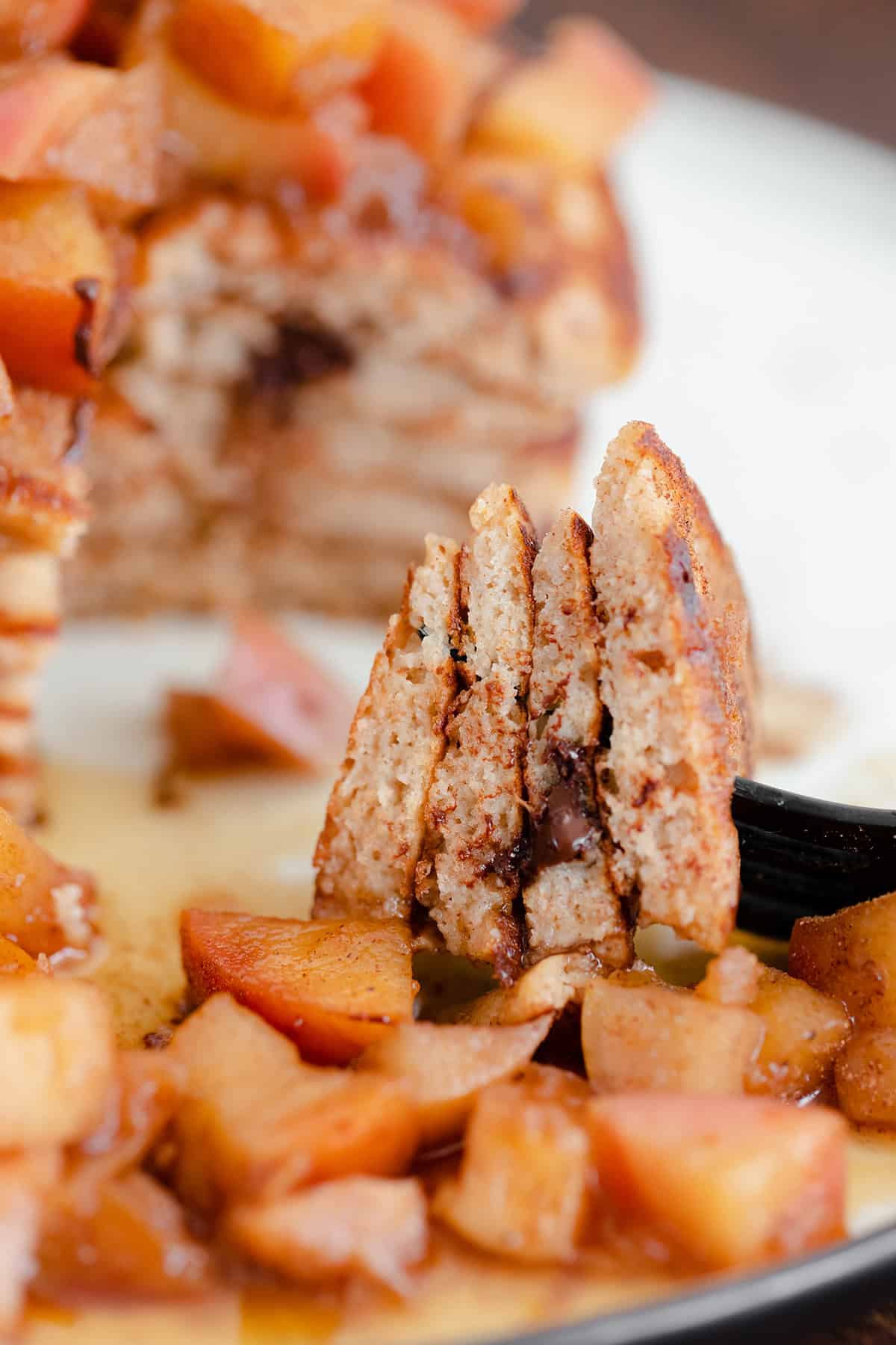 A straight on photo of Chocolate Chip Apple Cider Pancakes with Stewed Apples on a white plate and dark wooden background.