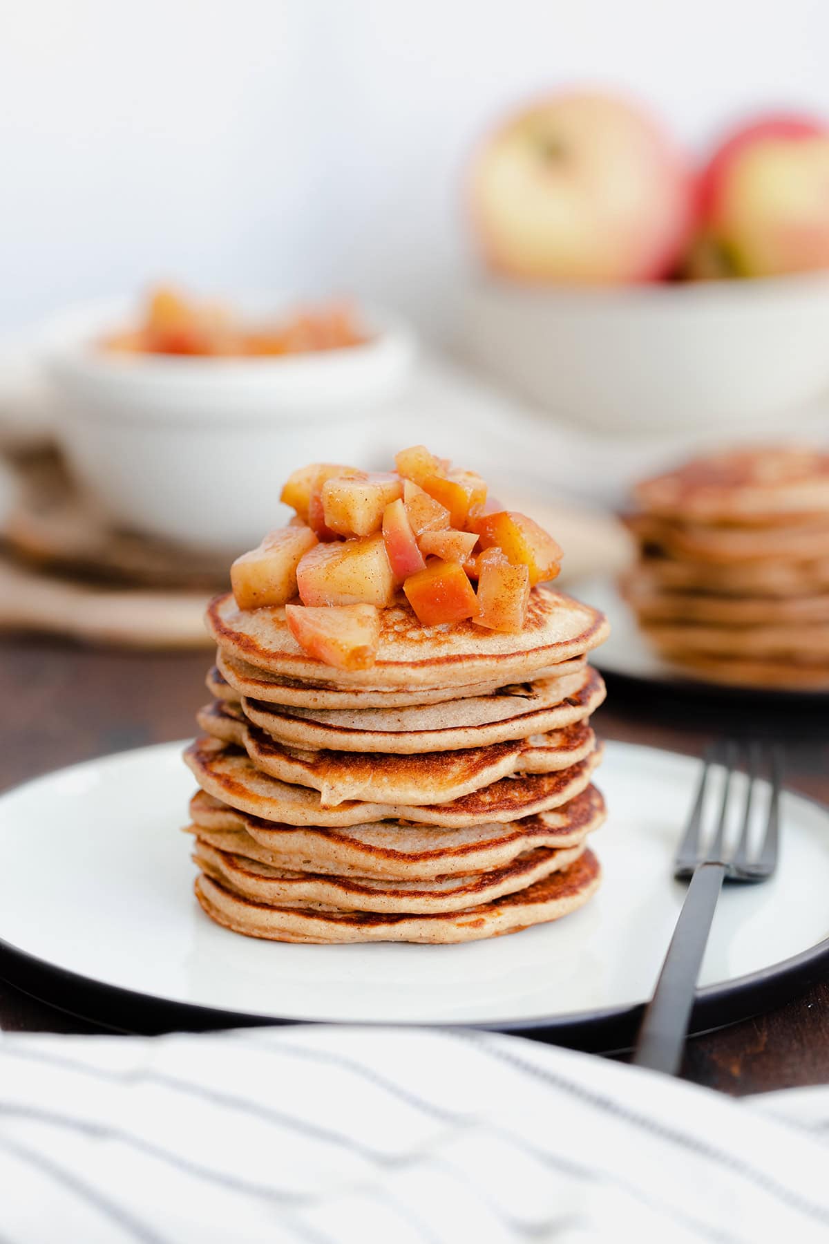 A straight on photo of Chocolate Chip Apple Cider Pancakes with Stewed Apples on a white plate and dark wooden background.