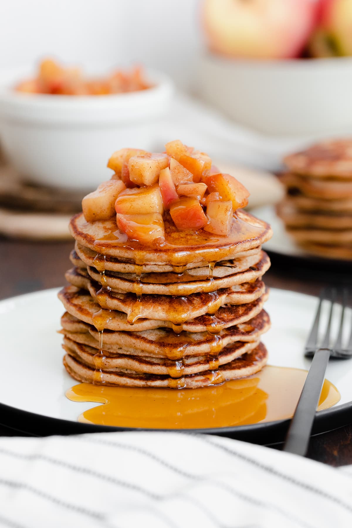 A straight on photo of Chocolate Chip Apple Cider Pancakes with Stewed Apples on a white plate and dark wooden background.