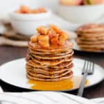 A straight on photo of Chocolate Chip Apple Cider Pancakes with Stewed Apples on a white plate and dark wooden background.