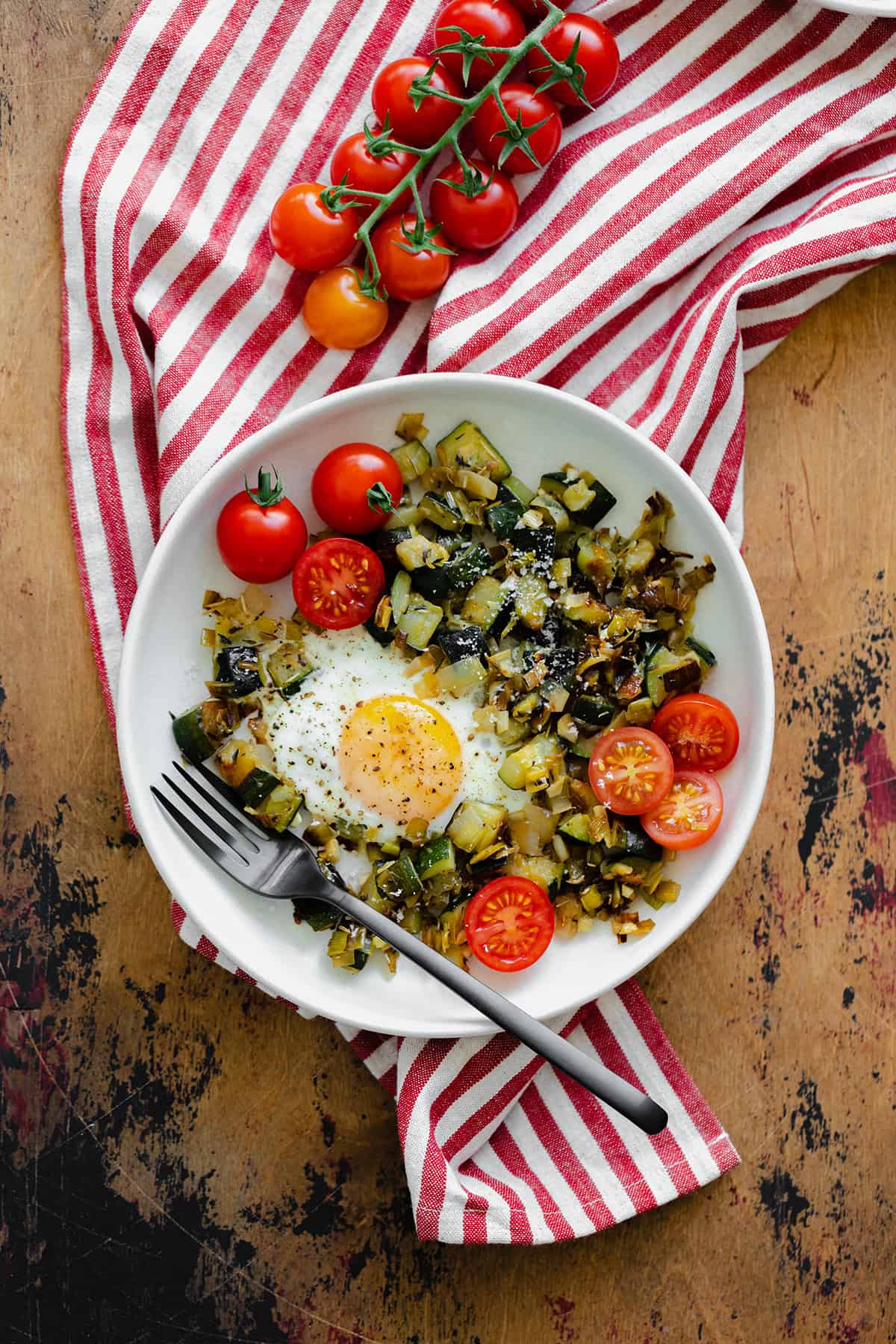 An overhead shot of Leek and Zucchini Egg Skillet on a red and white striped kitchen towel and wooden table