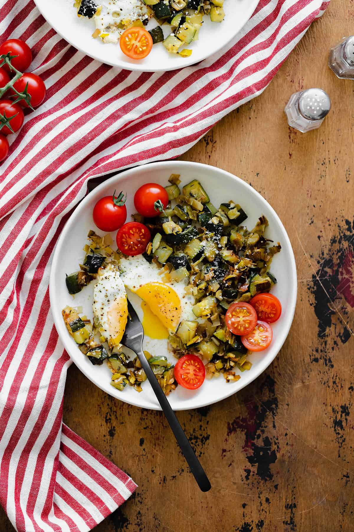 An overhead shot of Leek and Zucchini Egg Skillet on a red and white striped kitchen towel and wooden table