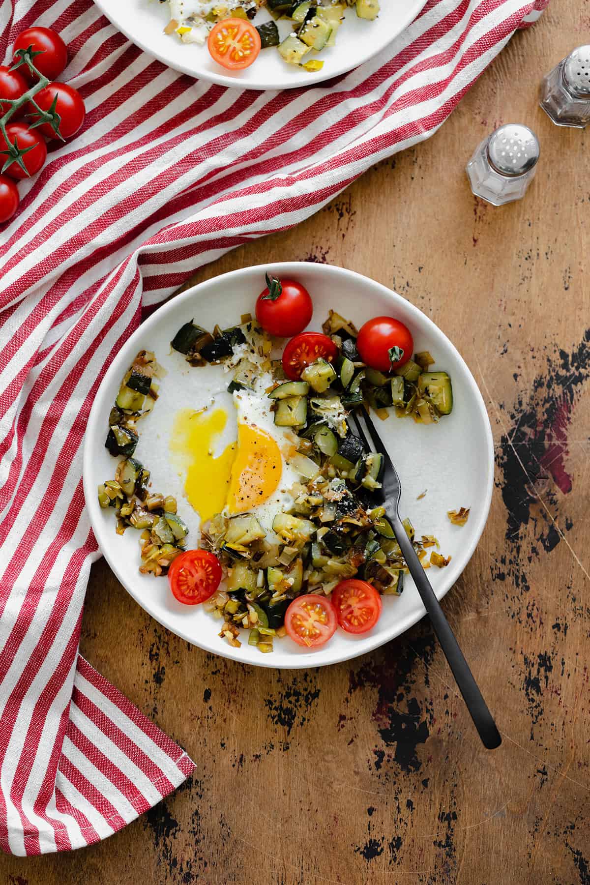 An overhead shot of Leek and Zucchini Egg Skillet on a red and white striped kitchen towel and wooden table