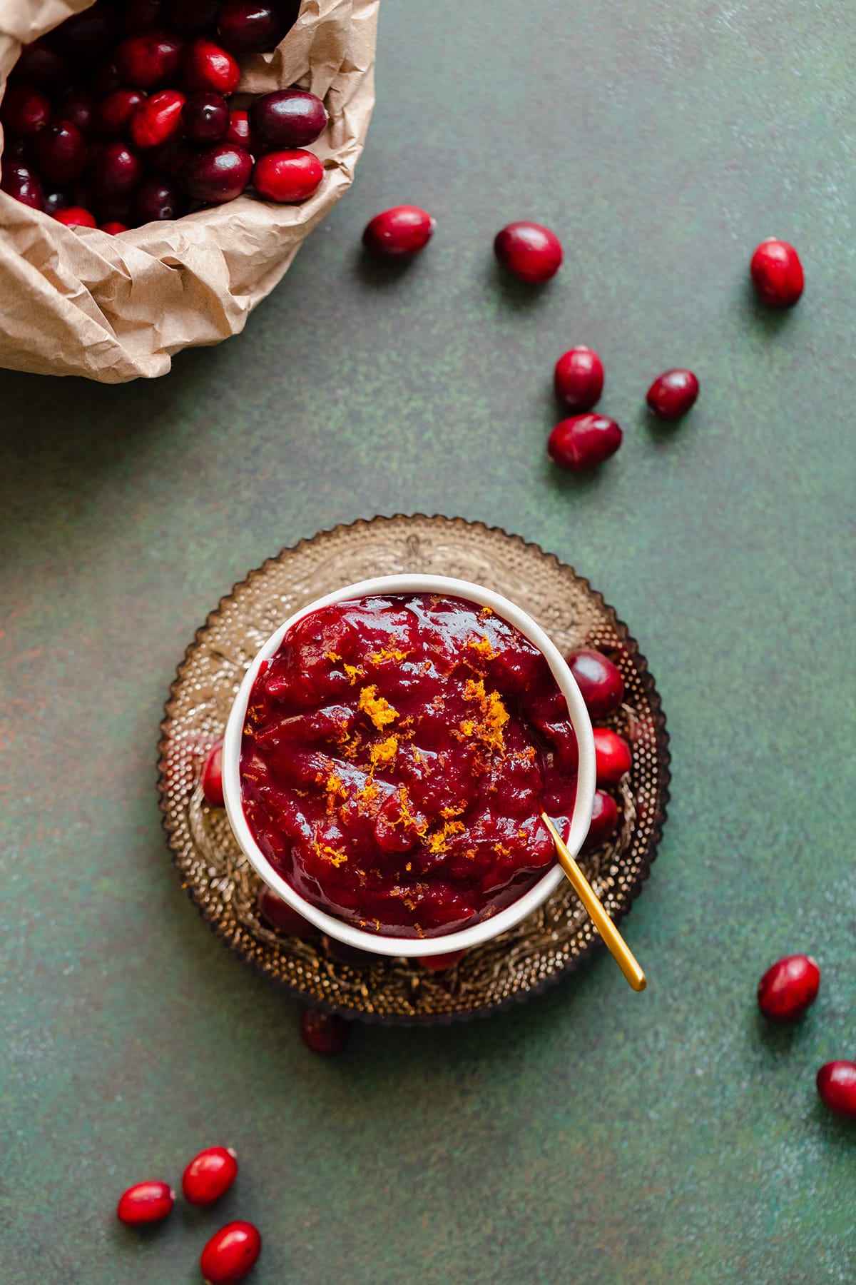 An overhead shot of Orange Maple Cranberry Sauce on a green background with a paper bag with fresh cranberries in the top left corner
