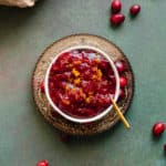 A square photo of Orange Maple Cranberry Sauce in a white bowl on green background