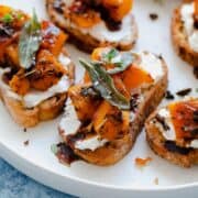 A photo of Butternut Squash Crostini with Goat Cheese and Fig Balsamic Glaze on a white plate