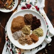 A photo of all the spices used in the Christmas Spice Blend on a white plate. On a dark wooden background.