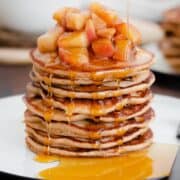 A straight on photo of Chocolate Chip Apple Cider Pancakes with Stewed Apples on a white plate and dark wooden background.