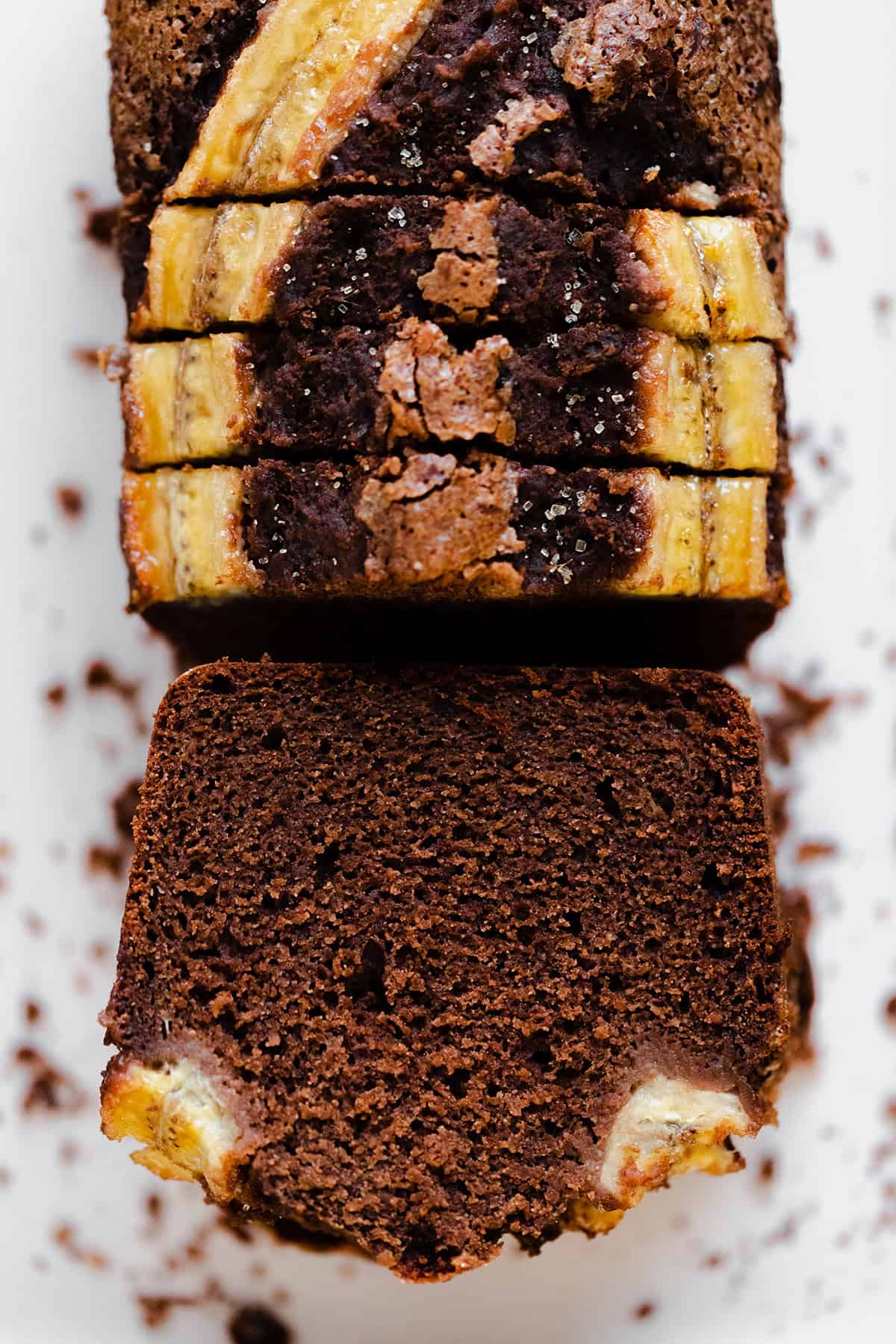 A photo of Caramelized Chocolate Banana Bread on a beige plate, green kitchen towel, and light wooden table.