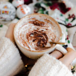 A shot of Christmas Spiced Hot Chocolate with whipped cream, dusted with gingerbread spice in a beige cup.