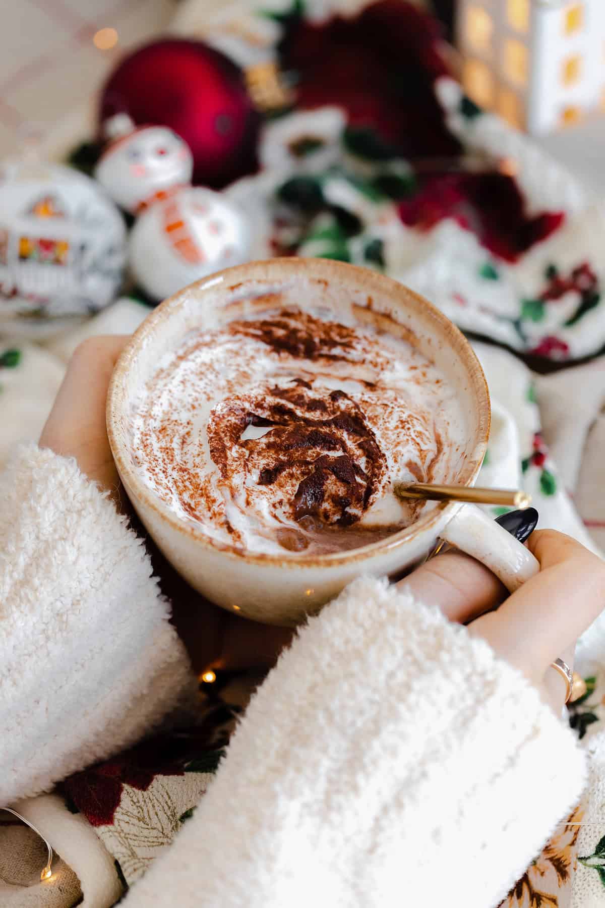 A shot of Christmas Spiced Hot Chocolate with whipped cream, dusted with gingerbread spice in a beige cup.