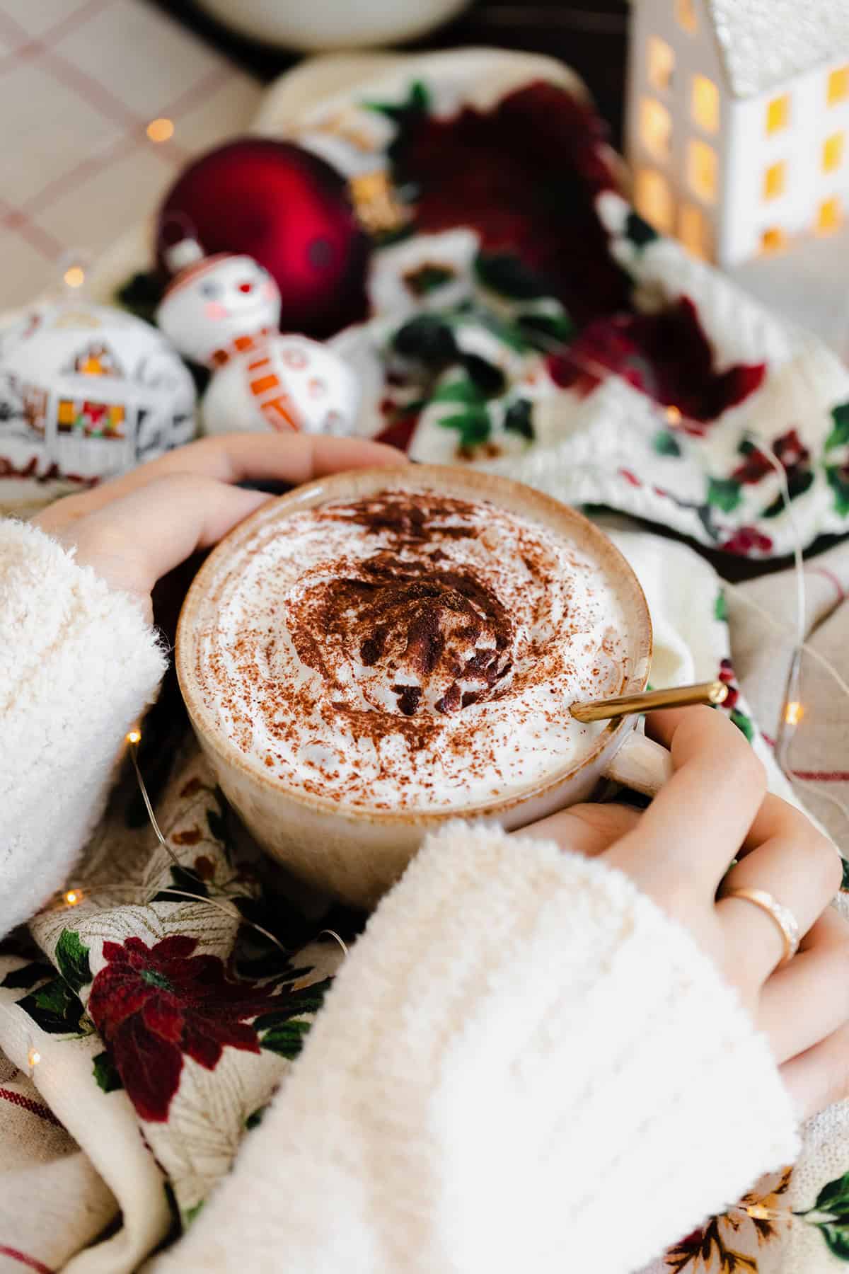 A shot of Christmas Spiced Hot Chocolate with whipped cream, dusted with gingerbread spice in a beige cup.