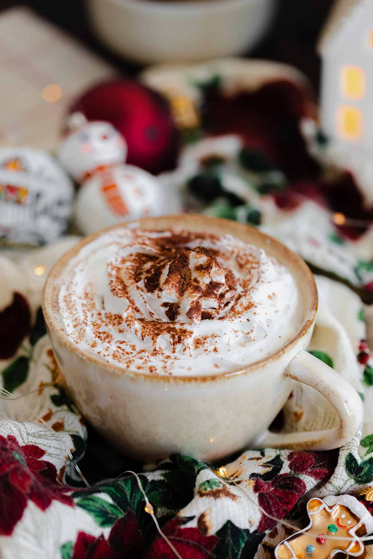 A shot of Christmas Spiced Hot Chocolate with whipped cream, dusted with gingerbread spice in a beige cup.