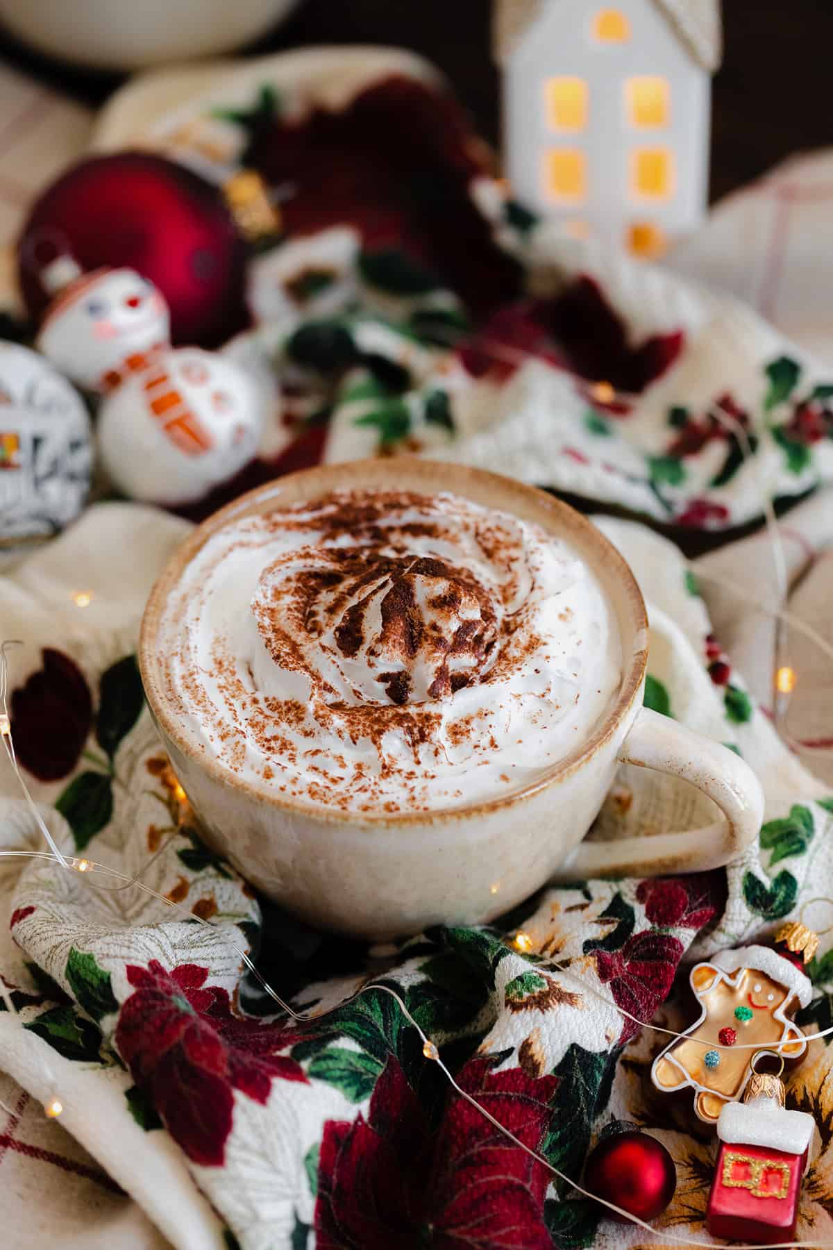 A shot of Christmas Spiced Hot Chocolate with whipped cream, dusted with gingerbread spice in a beige cup.