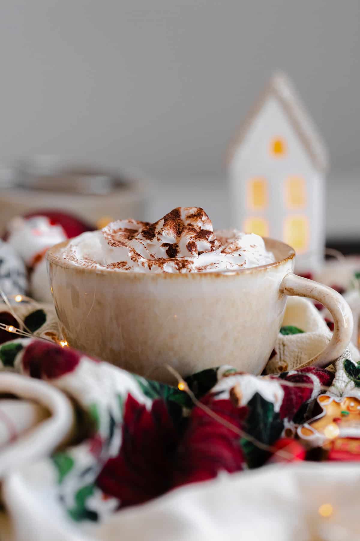 A shot of Christmas Spiced Hot Chocolate with whipped cream, dusted with gingerbread spice in a beige cup.