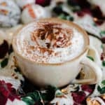 A shot of Christmas Spiced Hot Chocolate with whipped cream, dusted with gingerbread spice in a beige cup.