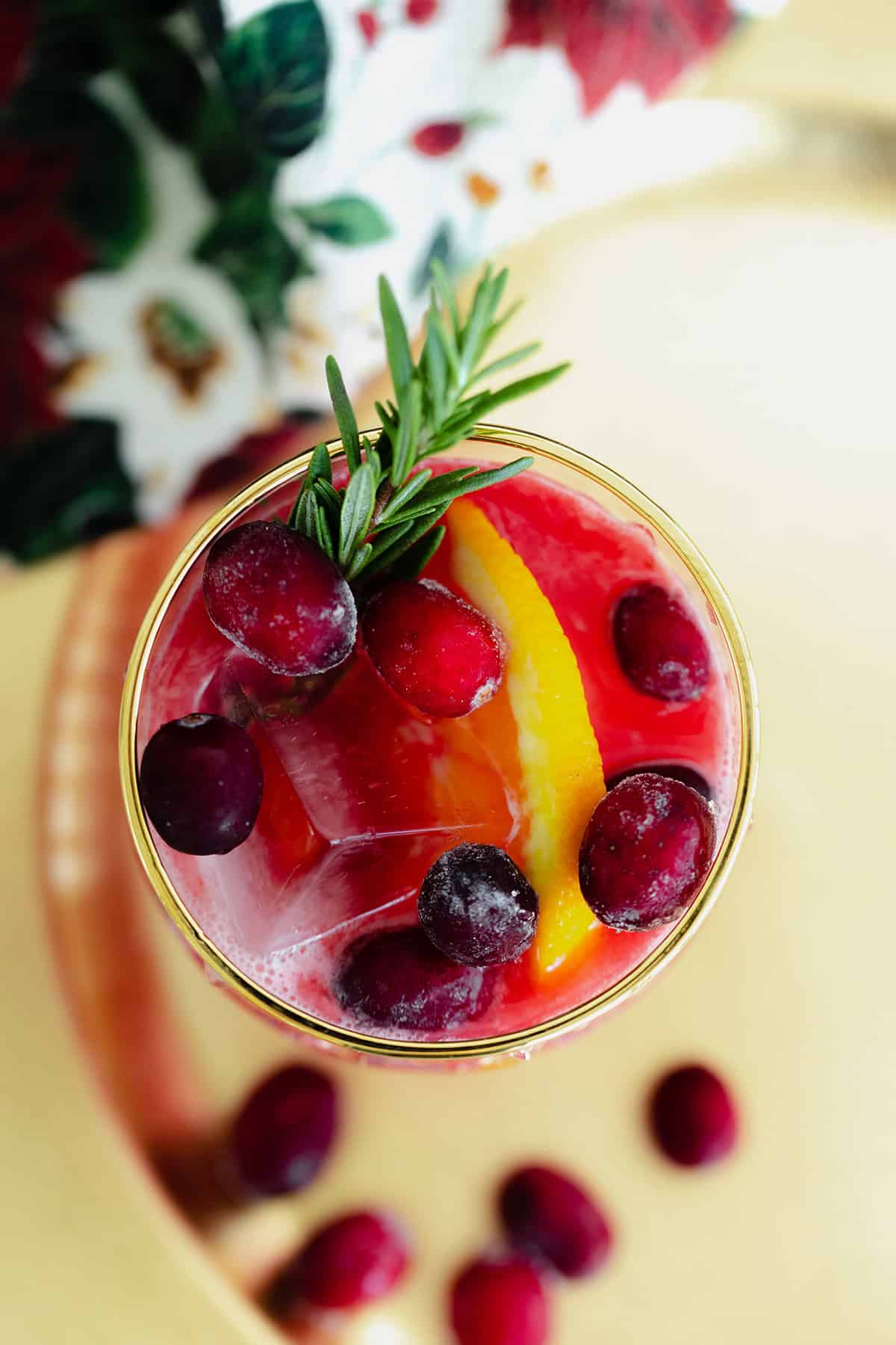 Cranberry Orange Margarita in a glass with a gold rim on a blue table with a black background.