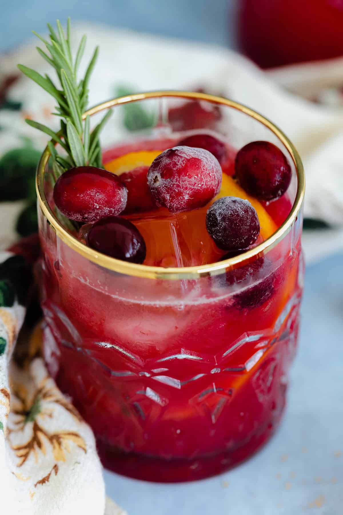 Cranberry Orange Margarita in a glass with a gold rim on a blue table with a black background.