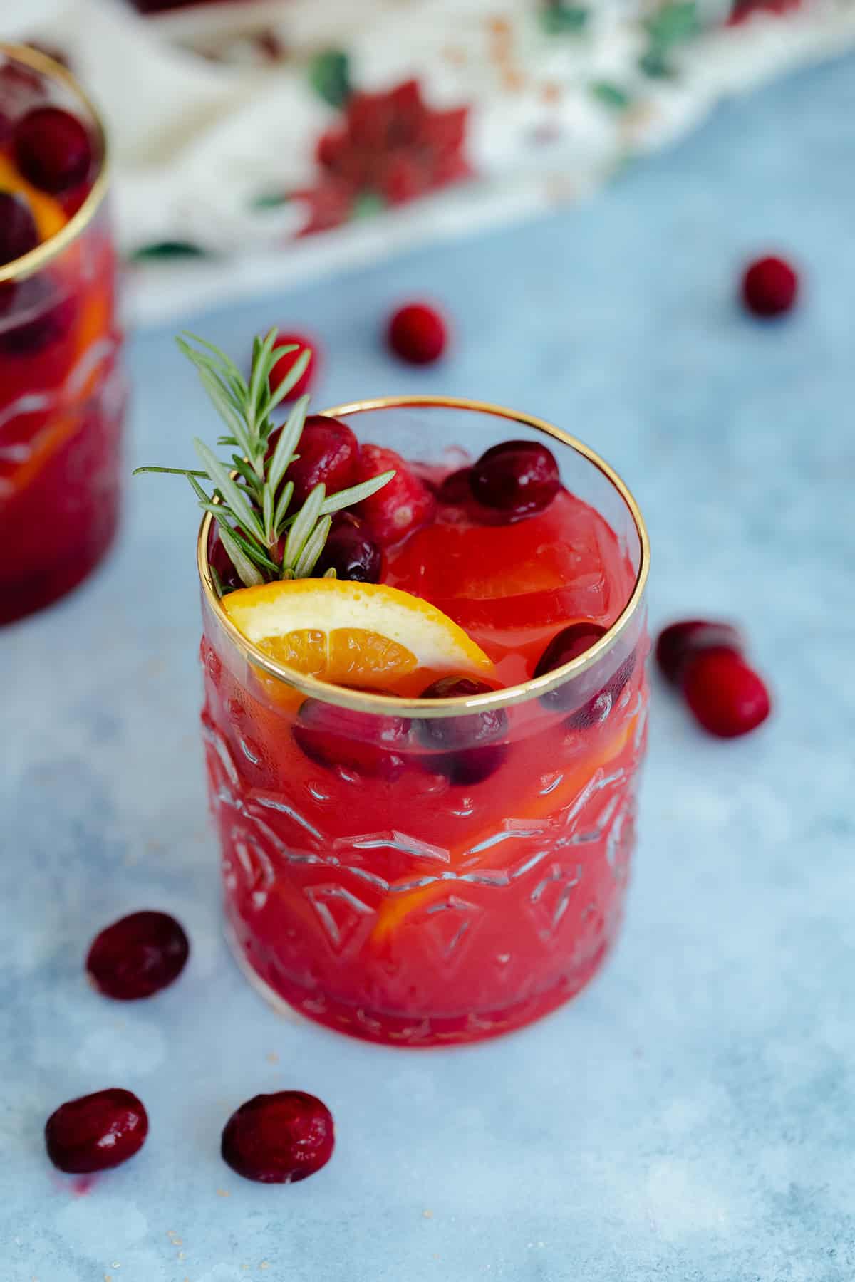 Cranberry Orange Margarita in a glass with a gold rim on a blue table with a black background.