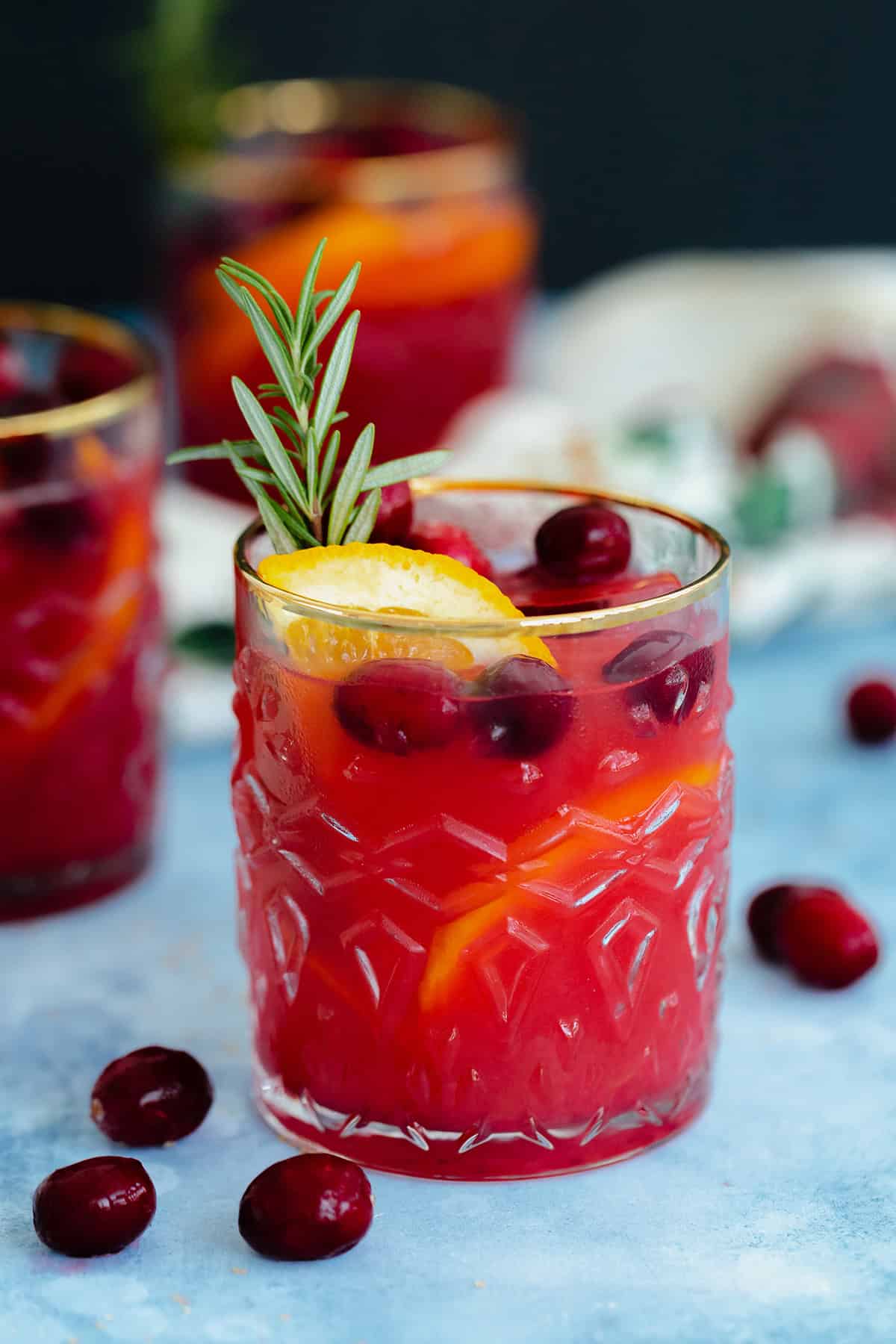 Cranberry Orange Margarita in a glass with a gold rim on a blue table with a black background.