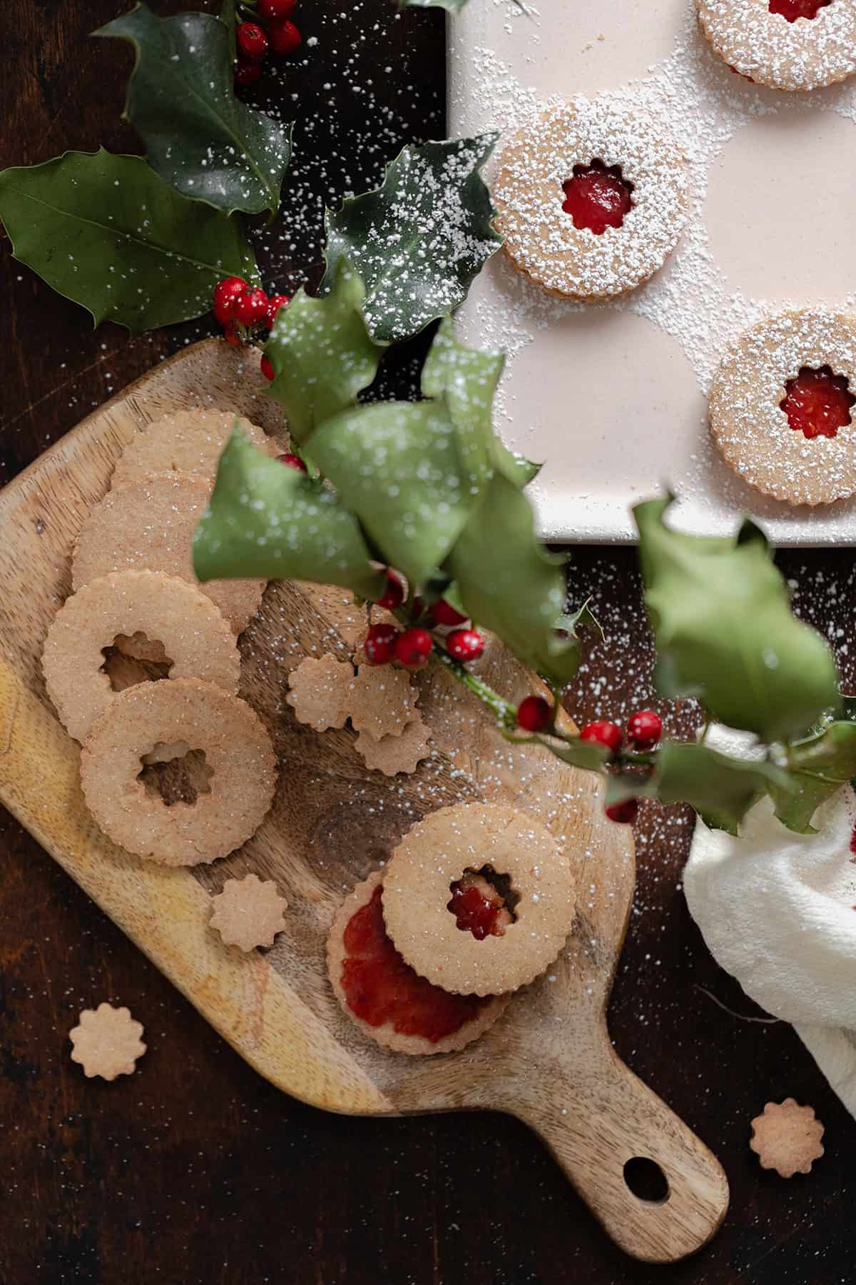 Linzer Cookies with raspberry jam and a dusting of powdered sugar on a wooden cutting board.