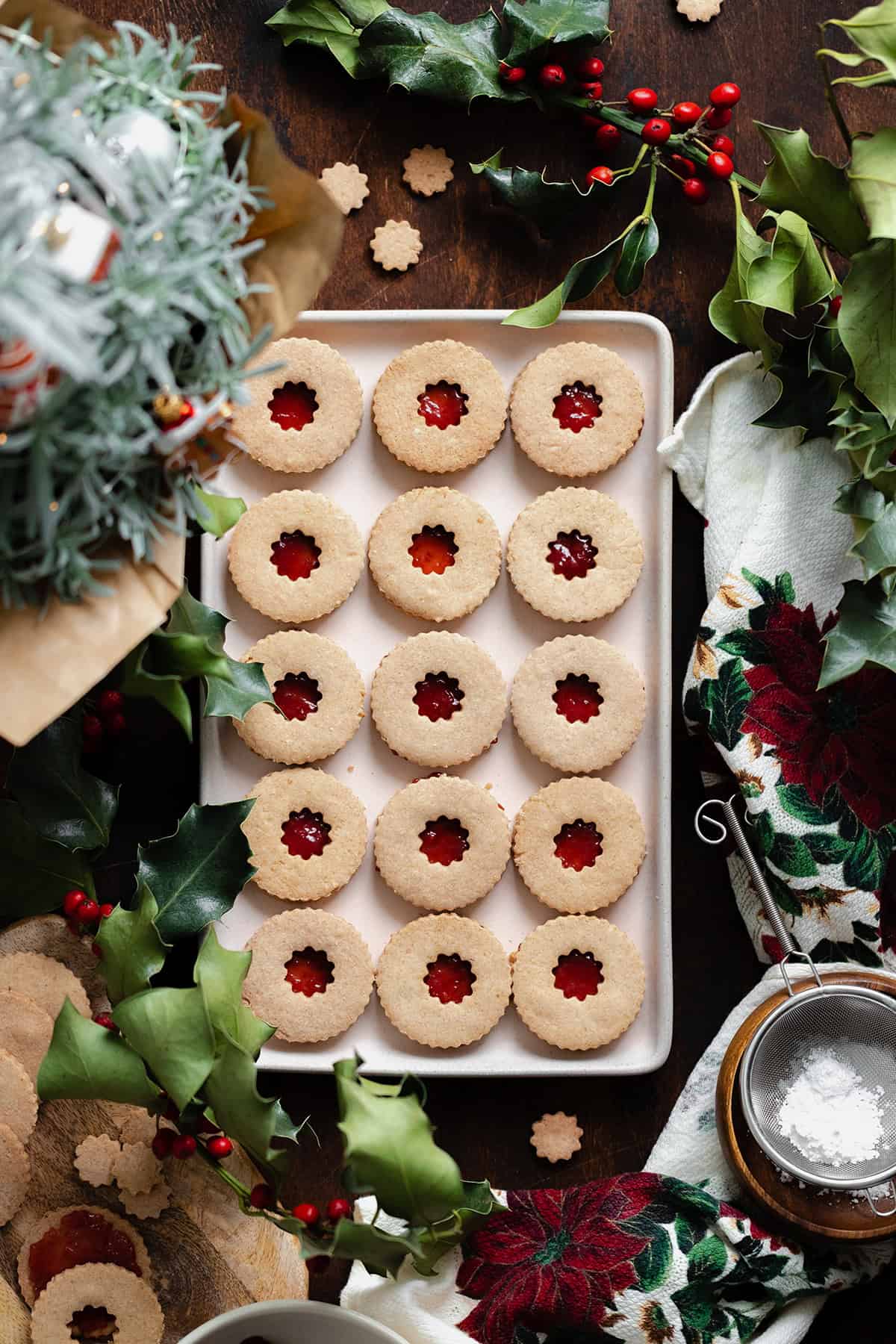 Gluten-Free Linzer Cookies with raspberry jam and on a beige plate. Decorated with Christmas decorations all around the plate