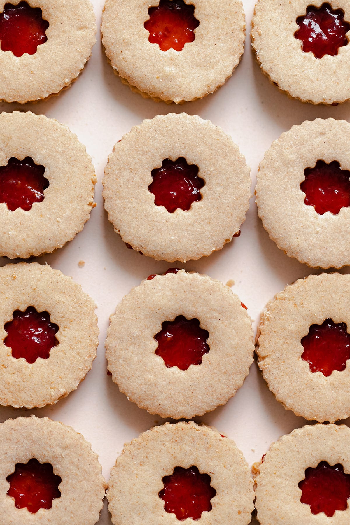 een close-up afbeelding van Linzer koekjes met frambozenjam op een beige bord. Koekjes zijn niet bestrooid met poedersuiker.